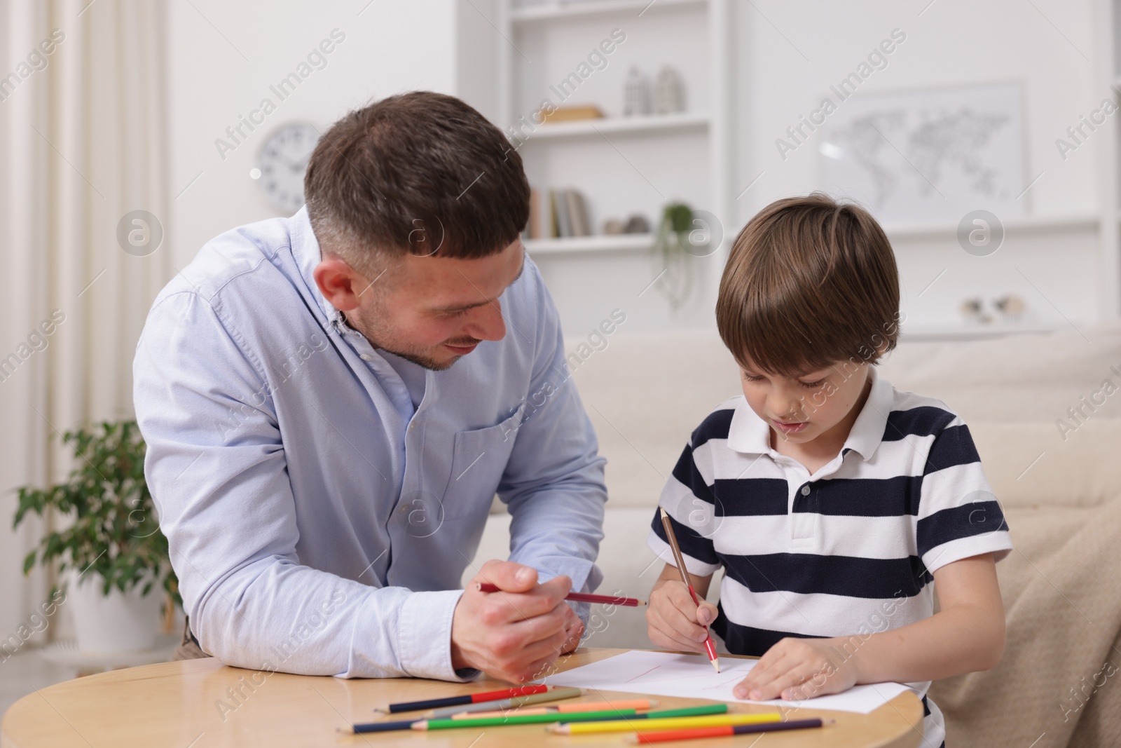 Father teaching his son to draw at table indoors Photo of Father teaching his son to draw at table indoors