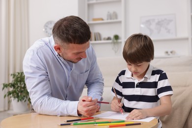 Photo of Father teaching his son to draw at table indoors