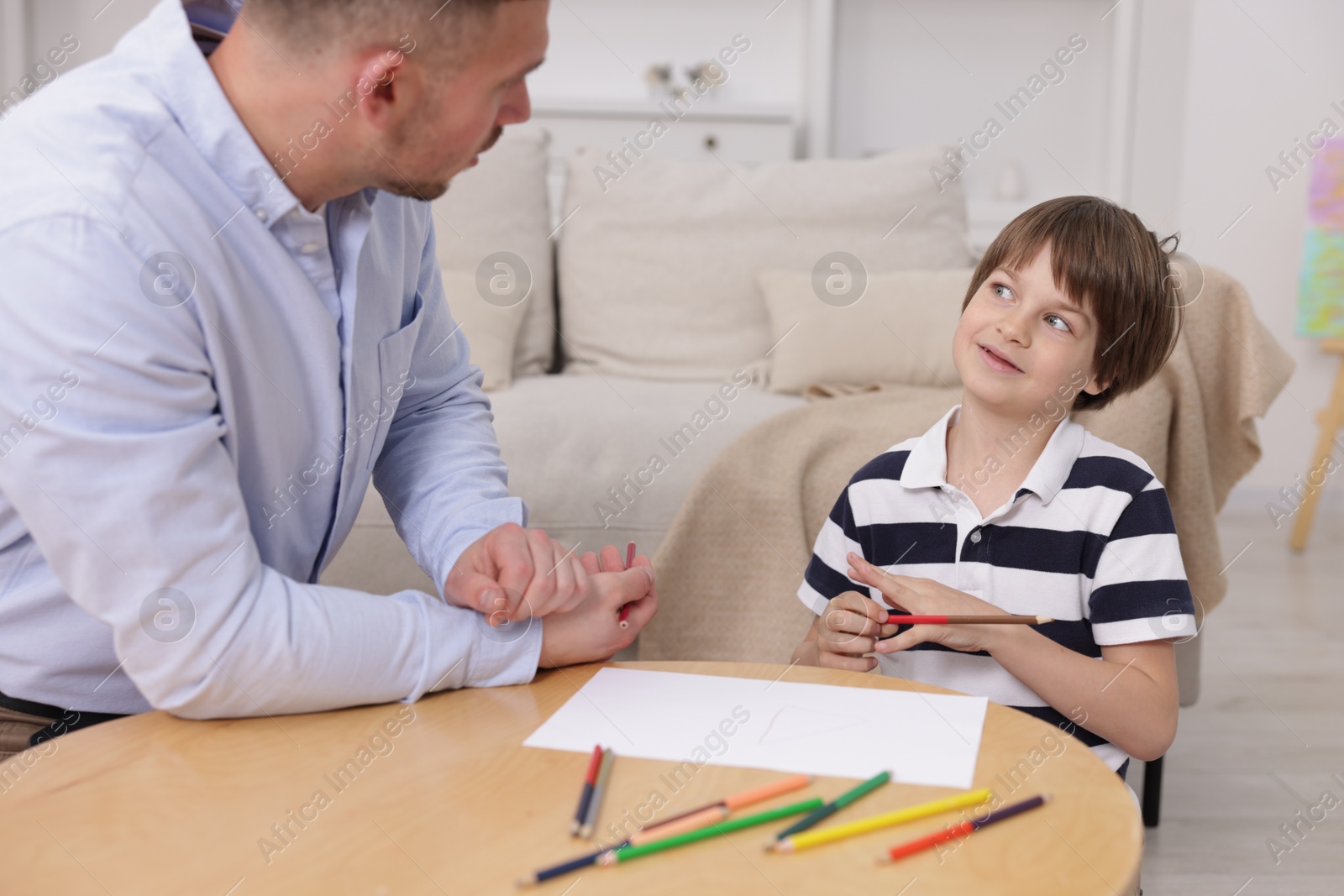 Father teaching his son to draw at table indoors Photo of Father teaching his son to draw at table indoors