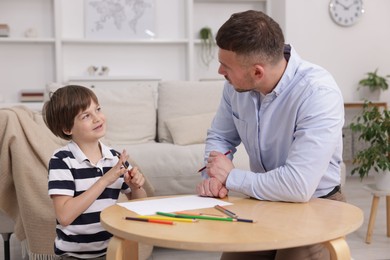 Photo of Father teaching his son to draw at table indoors