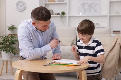 Photo of Father teaching his son to draw at table indoors