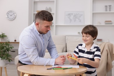 Photo of Father teaching his son to draw at table indoors