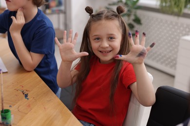 Photo of Cute little girl showing painted palms at lesson indoors. Learning to draw