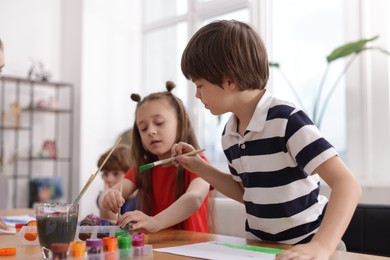 Photo of Kids painting at table indoors, selective focus. Learning to draw