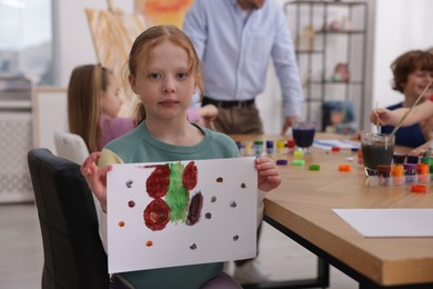 Photo of Cute little girl showing her painting at lesson indoors, selective focus. Learning to draw