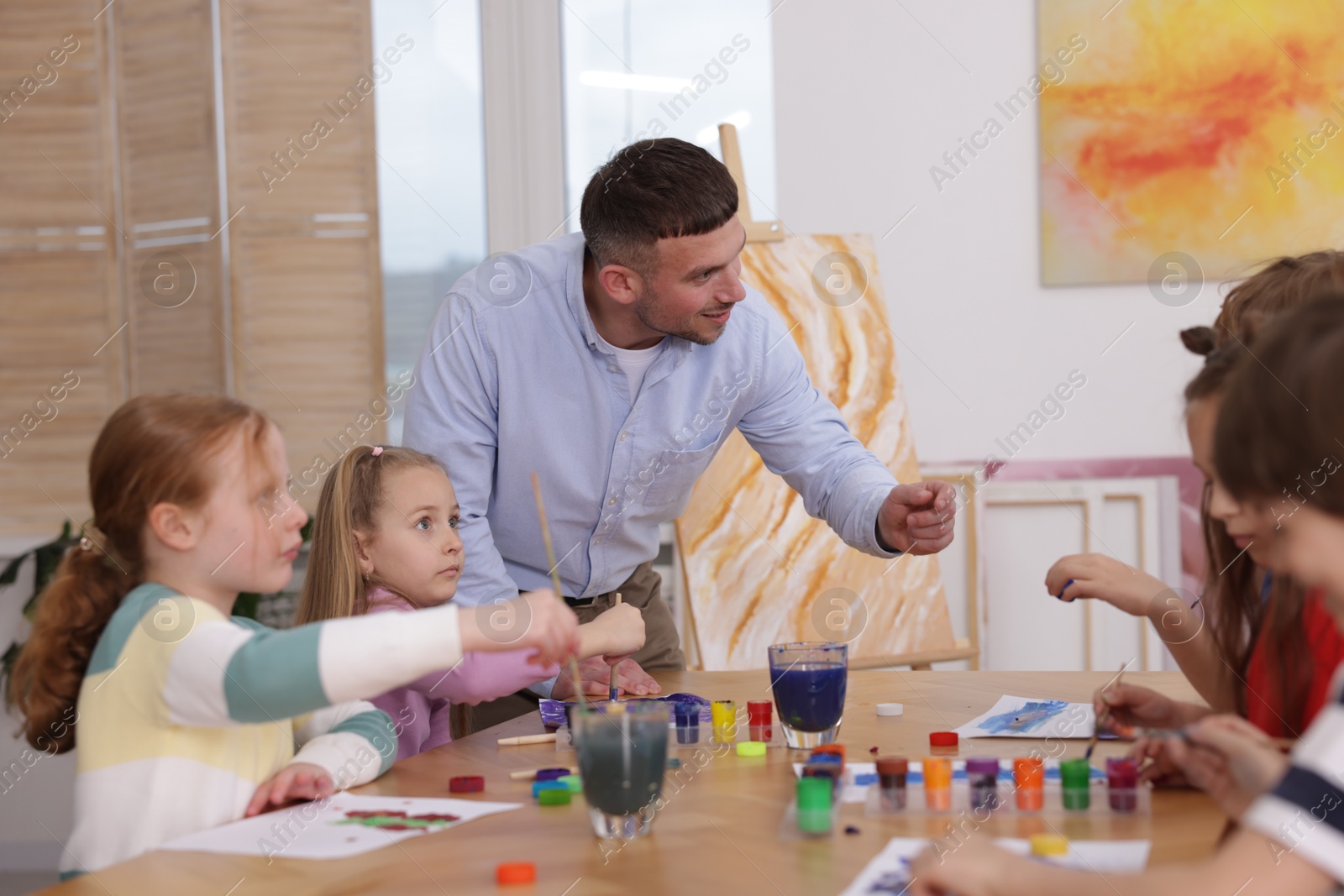 Man teaching kids to draw at painting lesson indoors Photo of Man teaching kids to draw at painting lesson indoors