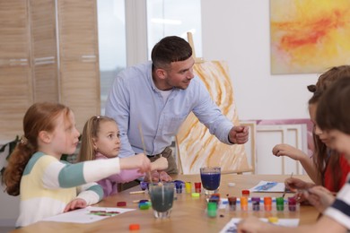 Photo of Man teaching kids to draw at painting lesson indoors