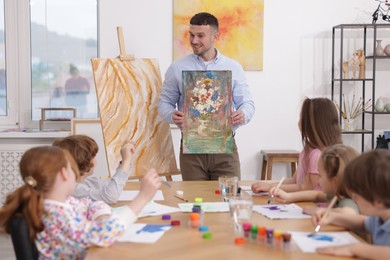 Photo of Man teaching kids to draw at painting lesson indoors