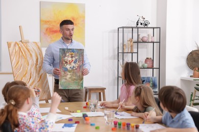 Photo of Man teaching kids to draw at painting lesson indoors