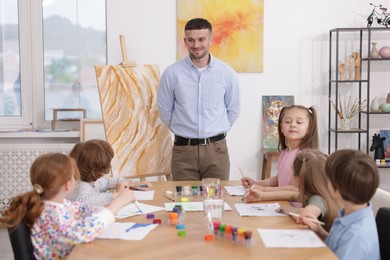 Photo of Man teaching kids to draw at painting lesson indoors