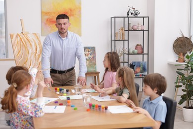 Photo of Man teaching kids to draw at painting lesson indoors