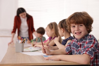 Photo of Woman teaching kids to draw at painting lesson indoors, selective focus