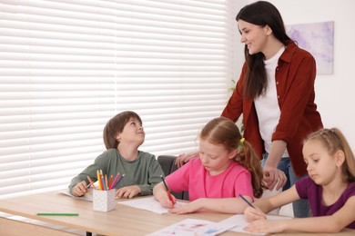 Photo of Woman teaching kids to draw at painting lesson indoors