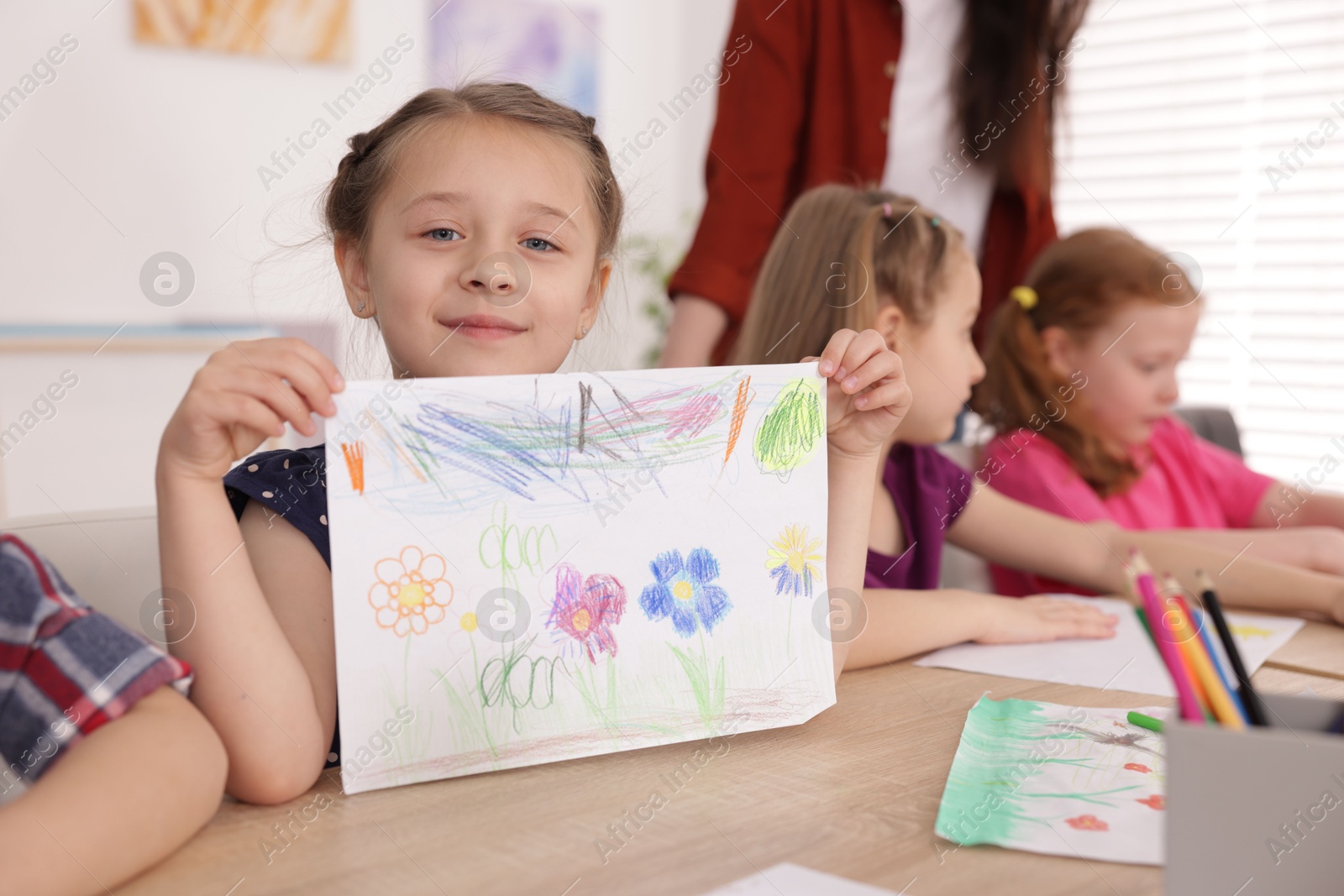 Cute girl showing her drawing during painting lesson indoors, selective focus Photo of Cute girl showing her drawing during painting lesson indoors, selective focus
