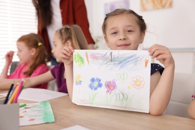 Photo of Cute girl showing her drawing during painting lesson indoors, selective focus