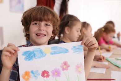 Photo of Cute boy showing his drawing during painting lesson indoors, selective focus