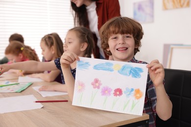 Photo of Cute boy showing his drawing during painting lesson indoors, selective focus