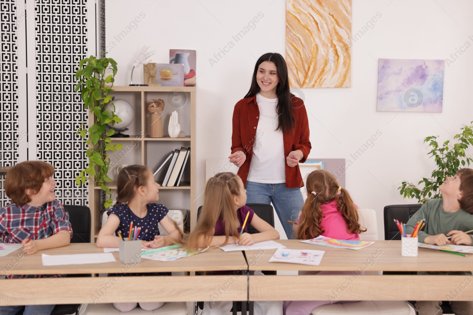 Woman teaching kids to draw at painting lesson indoors Photo of Woman teaching kids to draw at painting lesson indoors