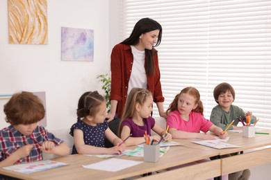 Photo of Woman teaching kids to draw at painting lesson indoors