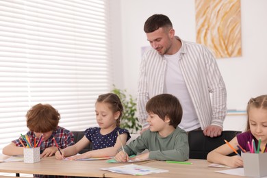 Photo of Man teaching kids to draw at painting lesson indoors