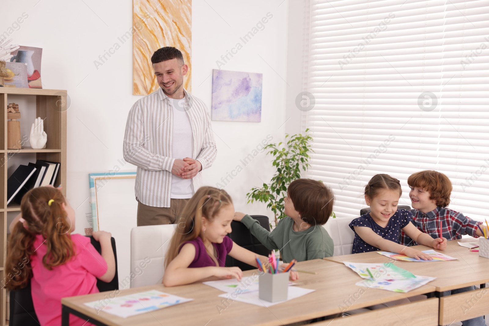Man teaching kids to draw at painting lesson indoors Photo of Man teaching kids to draw at painting lesson indoors