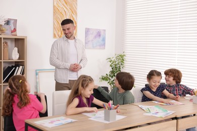 Photo of Man teaching kids to draw at painting lesson indoors