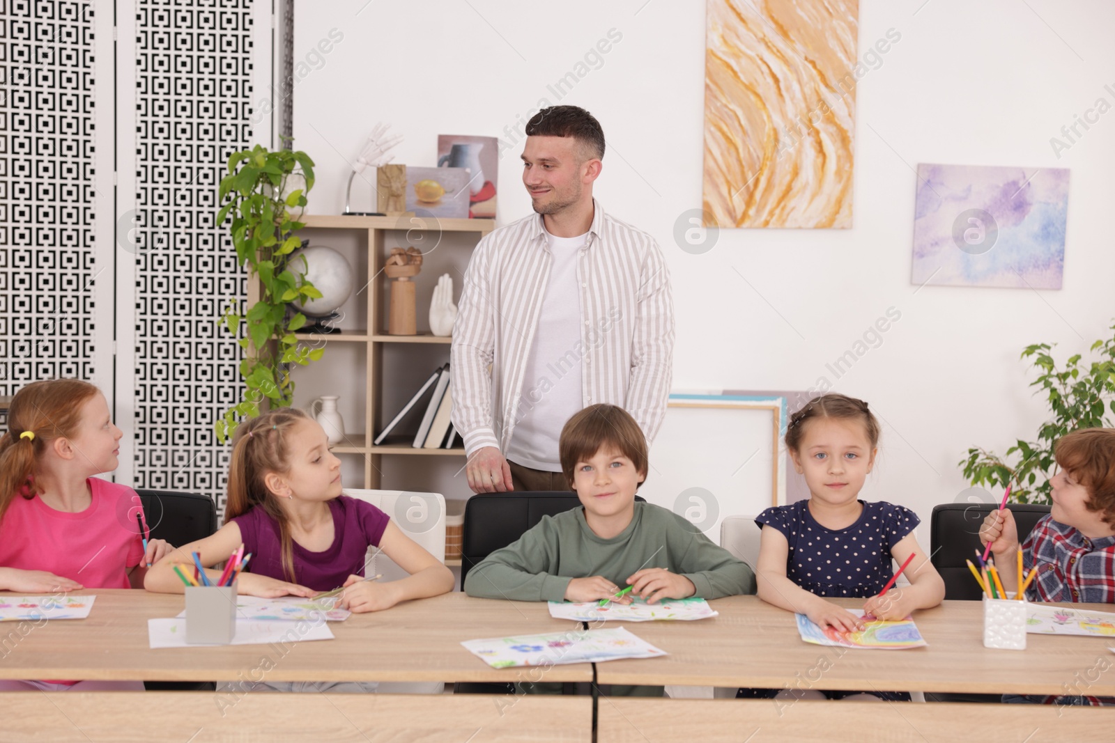 Man teaching kids to draw at painting lesson indoors Photo of Man teaching kids to draw at painting lesson indoors