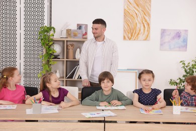 Photo of Man teaching kids to draw at painting lesson indoors