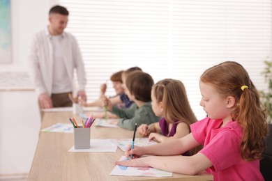 Photo of Man teaching kids to draw at painting lesson indoors, selective focus
