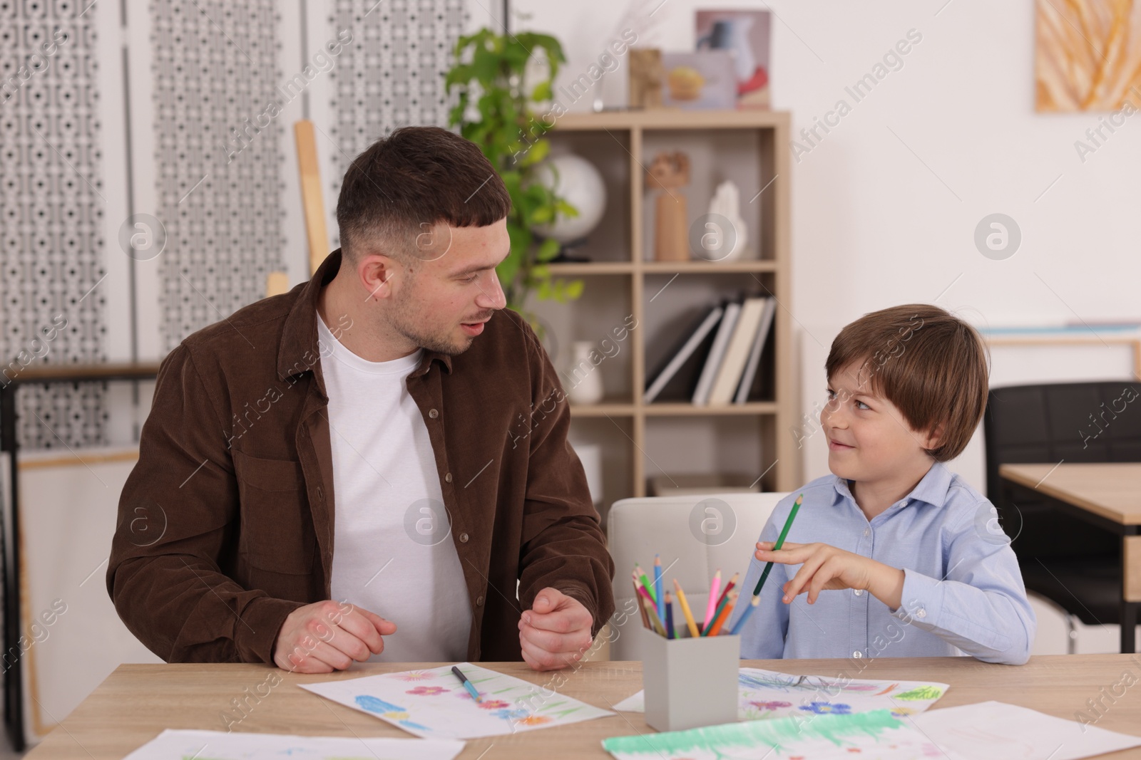 Man teaching kid to draw at painting lesson indoors Photo of Man teaching kid to draw at painting lesson indoors