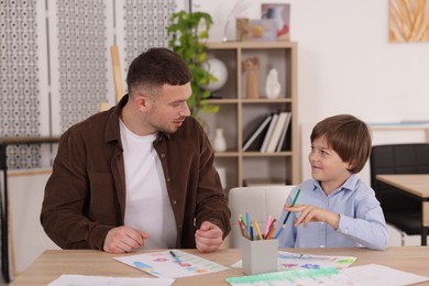 Photo of Man teaching kid to draw at painting lesson indoors