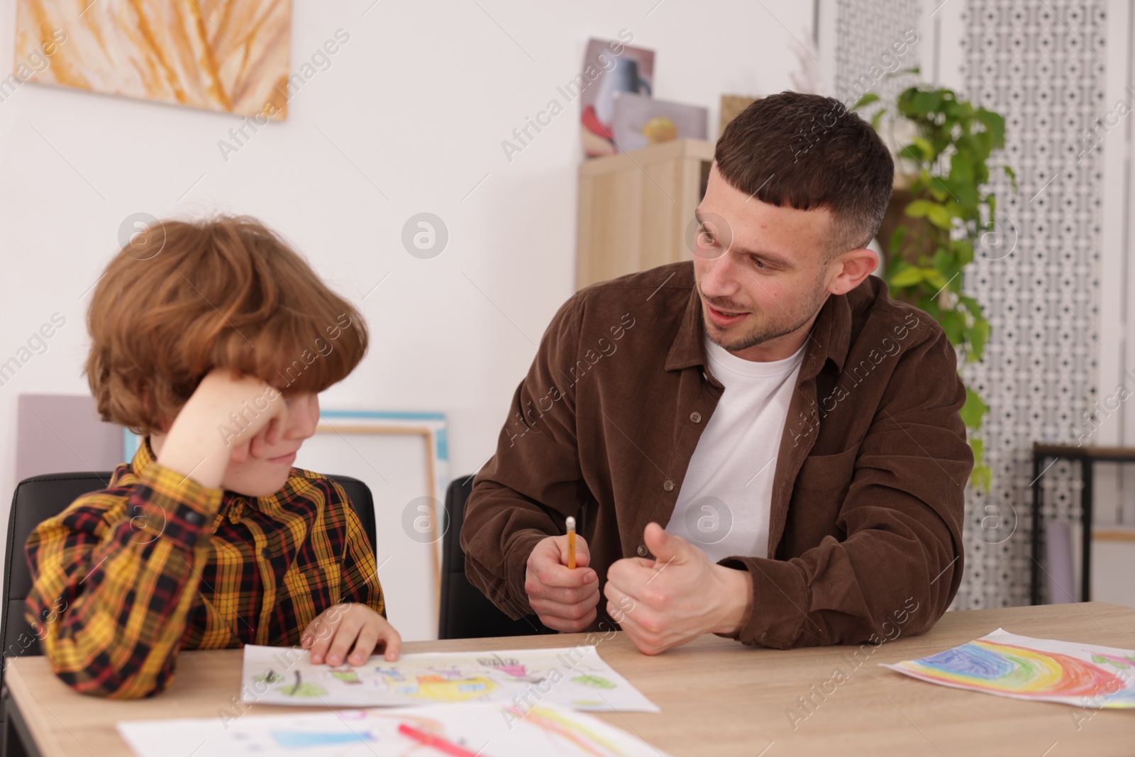 Man teaching kid to draw at painting lesson indoors Photo of Man teaching kid to draw at painting lesson indoors