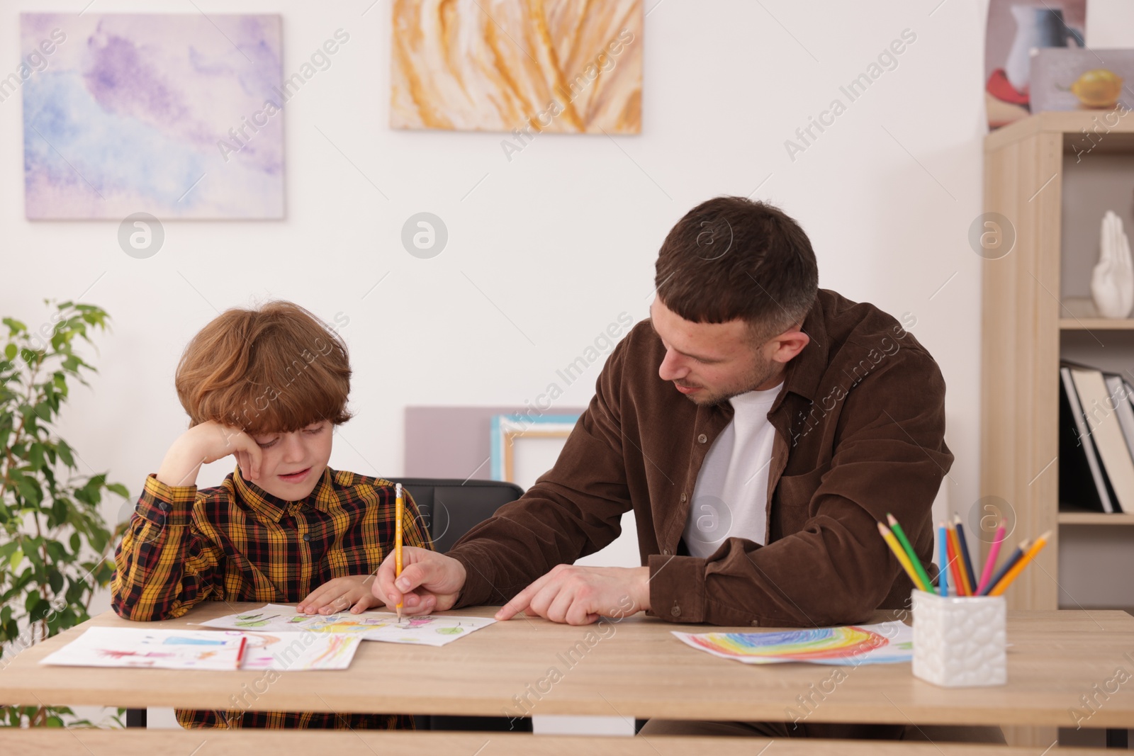 Man teaching kid to draw at painting lesson indoors Photo of Man teaching kid to draw at painting lesson indoors