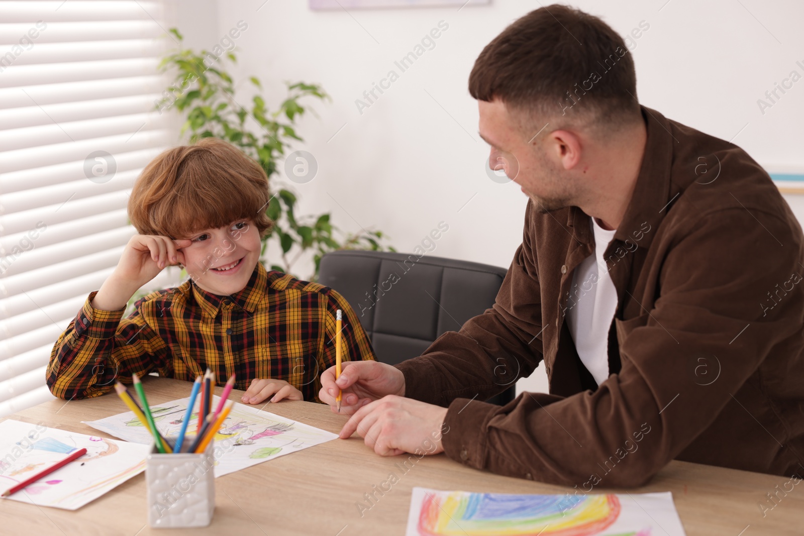 Man teaching kid to draw at painting lesson indoors Photo of Man teaching kid to draw at painting lesson indoors