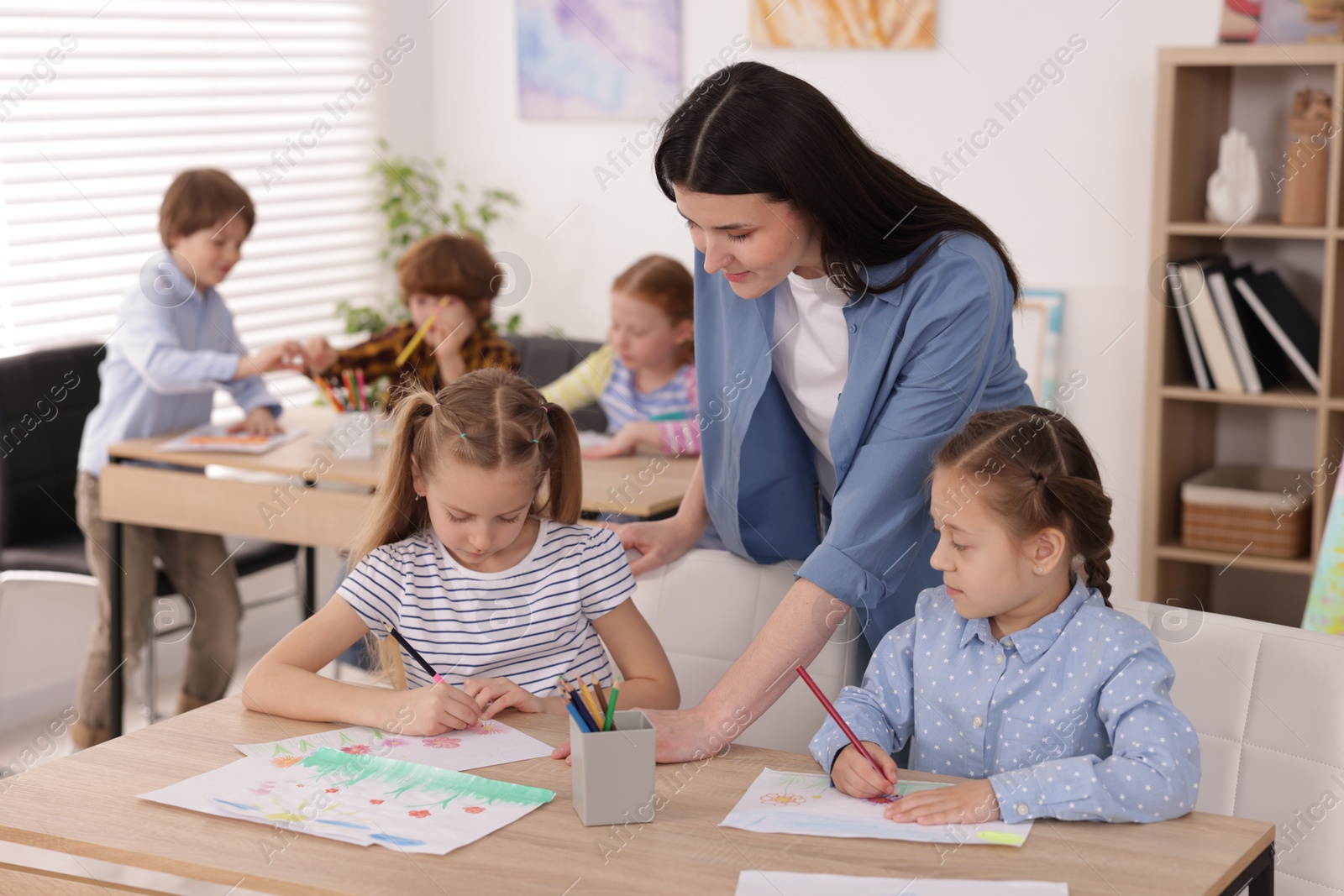 Woman teaching kids to draw at painting lesson indoors, selective focus Photo of Woman teaching kids to draw at painting lesson indoors, selective focus