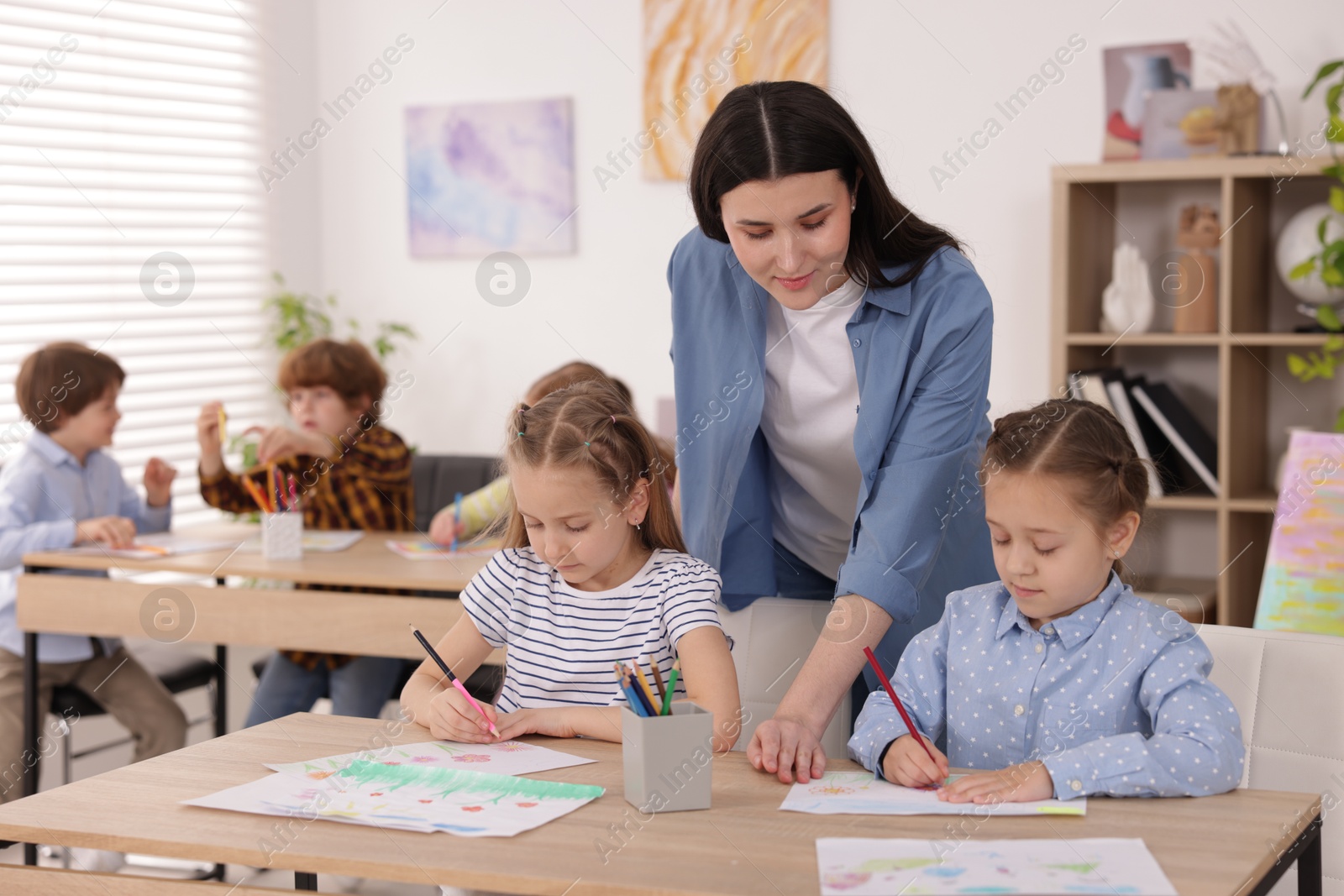 Woman teaching kids to draw at painting lesson indoors, selective focus Photo of Woman teaching kids to draw at painting lesson indoors, selective focus