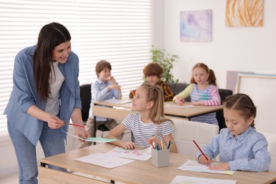 Photo of Woman teaching kids to draw at painting lesson indoors, selective focus