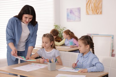 Photo of Woman teaching kids to draw at painting lesson indoors, selective focus