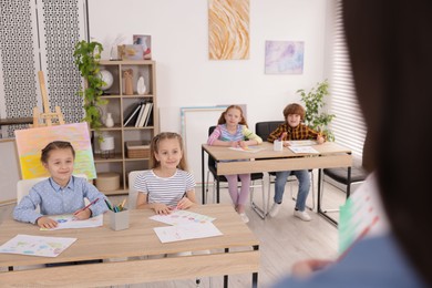 Photo of Woman teaching kids to draw at painting lesson indoors, selective focus