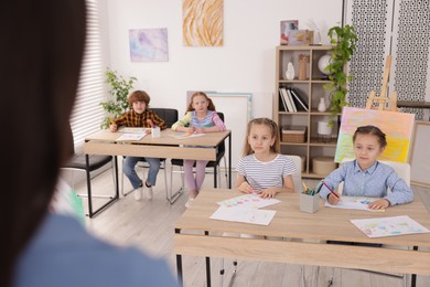 Photo of Woman teaching kids to draw at painting lesson indoors, selective focus