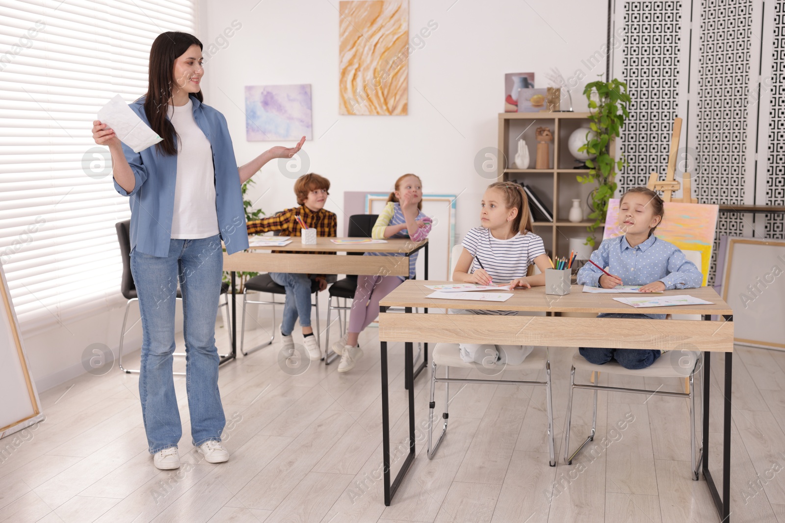 Woman teaching kids to draw at painting lesson indoors Photo of Woman teaching kids to draw at painting lesson indoors