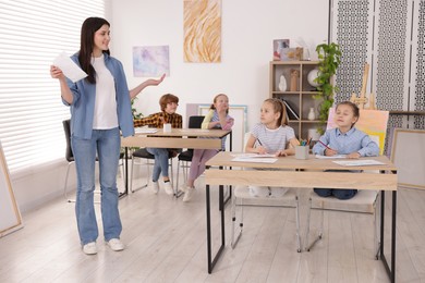 Photo of Woman teaching kids to draw at painting lesson indoors