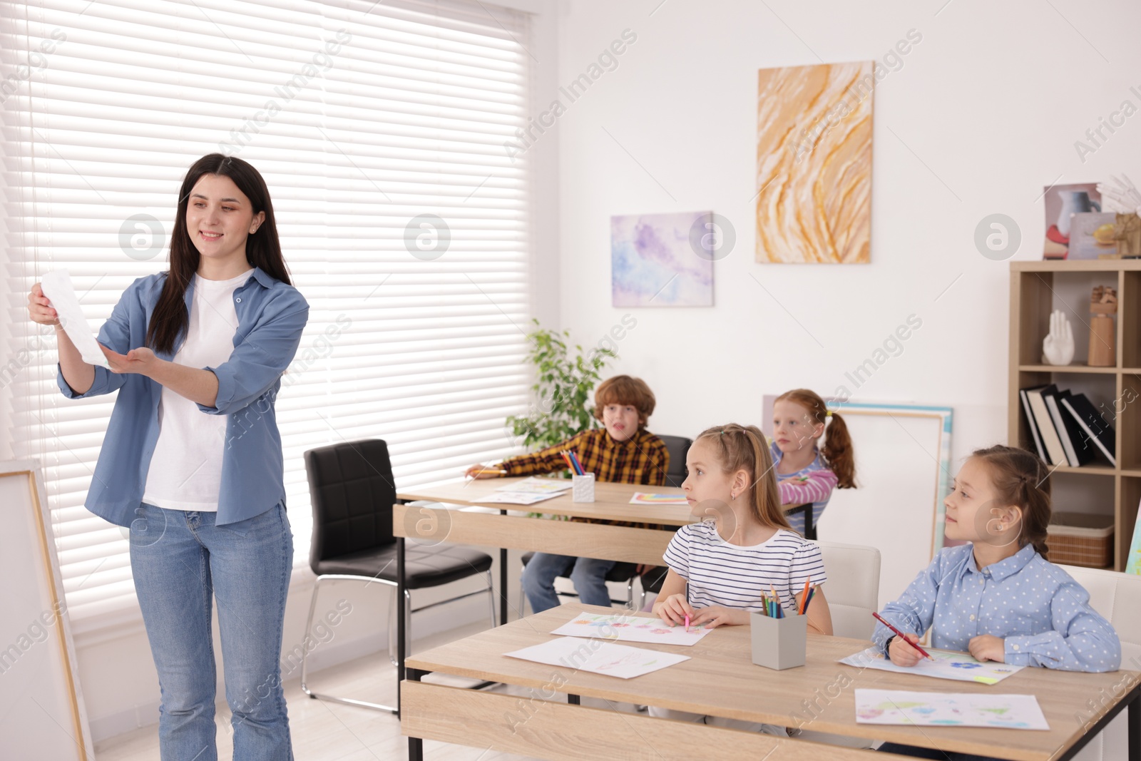 Woman teaching kids to draw at painting lesson indoors Photo of Woman teaching kids to draw at painting lesson indoors