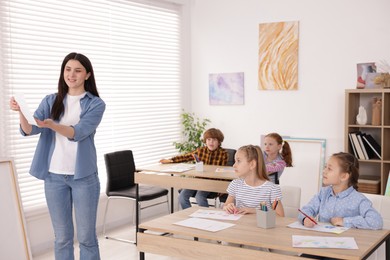 Photo of Woman teaching kids to draw at painting lesson indoors