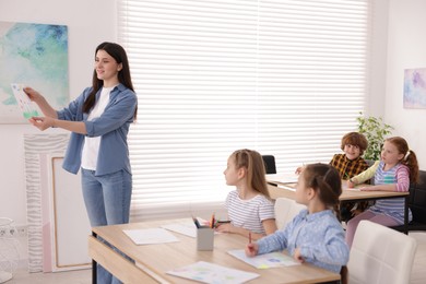 Photo of Woman teaching kids to draw at painting lesson indoors