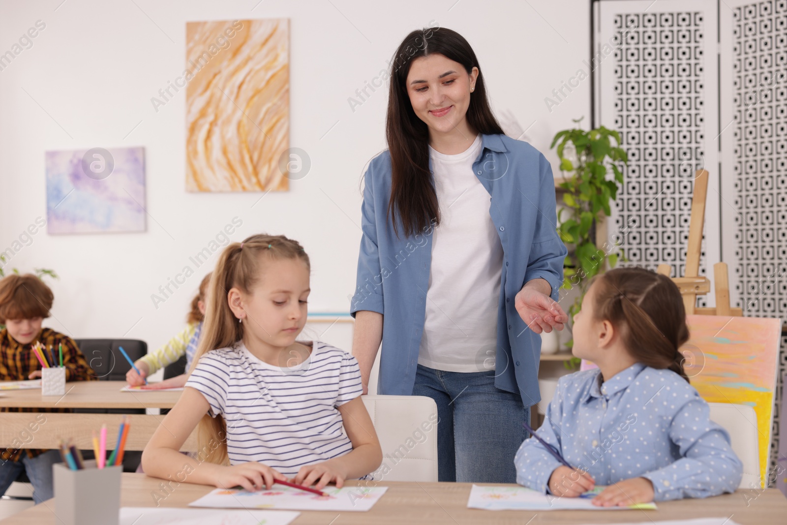 Woman teaching kids to draw at painting lesson indoors Photo of Woman teaching kids to draw at painting lesson indoors