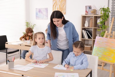 Photo of Woman teaching kids to draw at painting lesson indoors