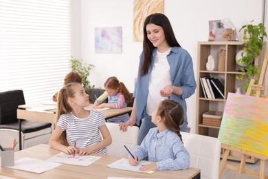 Photo of Woman teaching kids to draw at painting lesson indoors