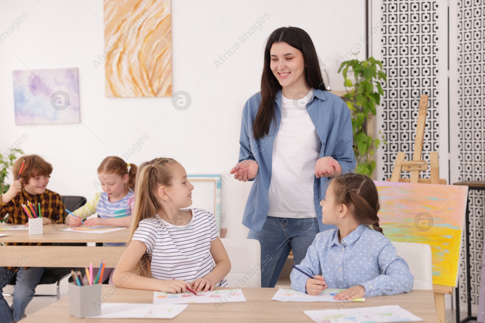 Woman teaching kids to draw at painting lesson indoors Photo of Woman teaching kids to draw at painting lesson indoors