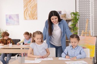 Photo of Woman teaching kids to draw at painting lesson indoors, selective focus